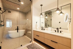 Ein modernes Badezimmer mit einer freistehenden Badewanne, einem großen Spiegel und Pendelleuchten.