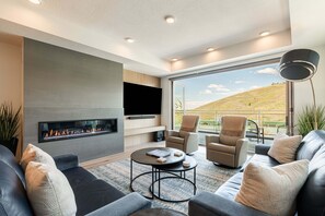 Una sala de estar moderna con chimenea, asientos cómodos, televisor de pantalla plana y un ventanal con vistas al exterior.