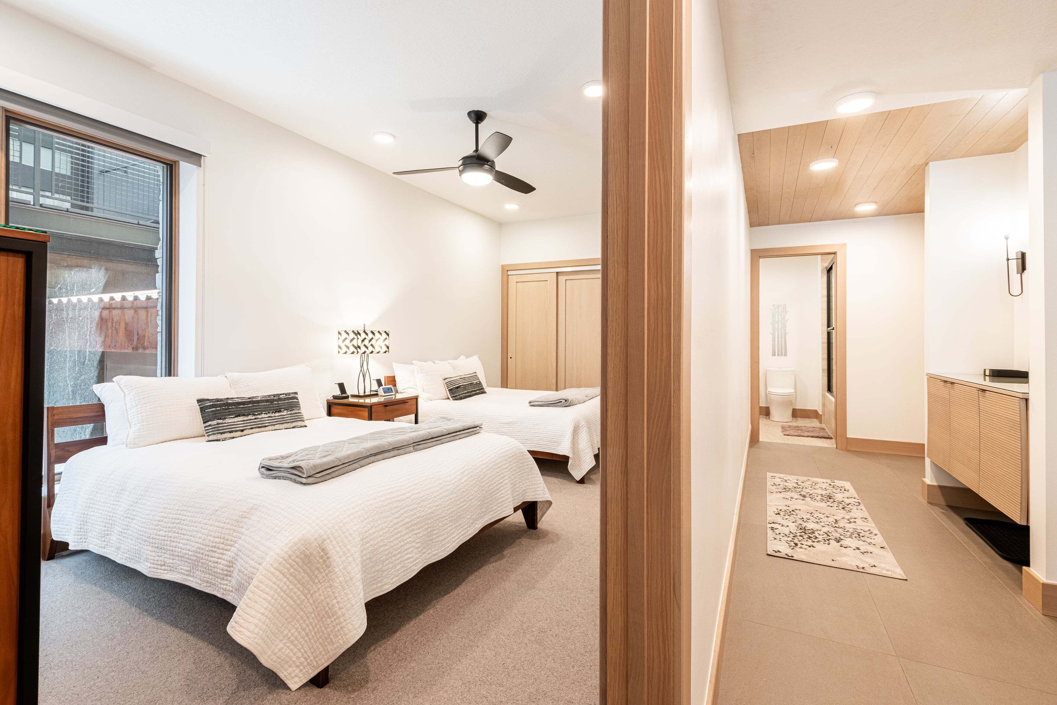 Een slaapkamer met twee bedden, een plafondventilator, een nachtkastje en uitzicht op een raam.