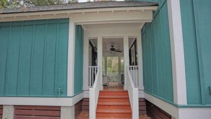 Een overdekte veranda met een houten trap naar een deur, omgeven door teal gevelbekleding.