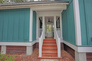 A covered porch with a wooden staircase leading to a door, surrounded by teal siding.