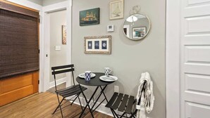 Een kamer met een houten vloer, een zwart inklapbaar tafeltje met twee stoelen, een ronde spiegel en kunstwerken aan de muur.