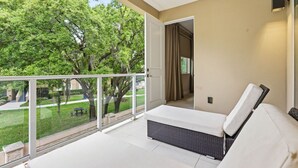 Un balcón con un sofá blanco, una silla de mimbre y vistas a un césped verde y árboles.
