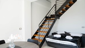 Een moderne slaapkamer met een bed, een rond tafeltje met een vaas en een trap.