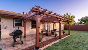 Eine überdachte Terrasse mit Gartenmöbeln, einem Grill und einem gepflegten Rasen.