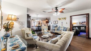 Ein Wohnzimmer mit Glastisch, Sofas, Deckenventilator und Essbereich im Hintergrund.