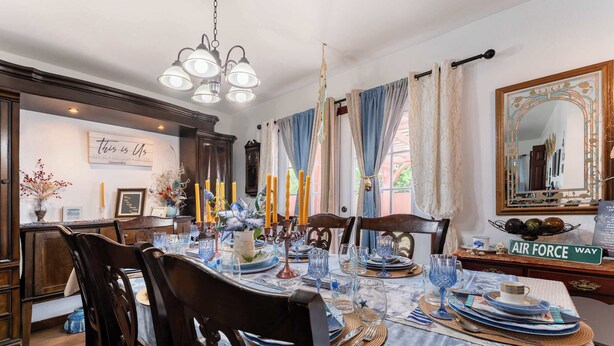 Ein Esszimmer mit einem runden Tisch, gedeckt für sechs Personen, Holzstühlen, einer Chandelierleuchtre und einem Wandspiegel.