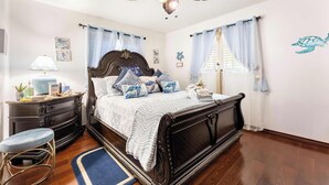 Ein Schlafzimmer mit einem Bett, einem Nachttisch, einer Lampe, einem Sessel und einem Deckenventilator.