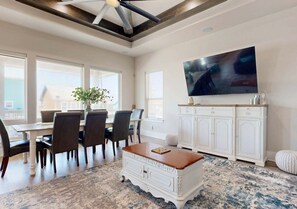 Un coin repas avec une table et des chaises, un meuble blanc, un téléviseur et un ventilateur de plafond.