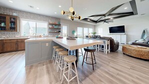 A spacious kitchen with a central island, bar stools, a dining area with a sofa, and a television. - PEL607 After Dune Delight, Private Heated Pool, Parking for 5 (Port Aransas)