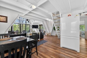 A modern interior with a dining area, a white refrigerator, and a staircase leading to an upper level.