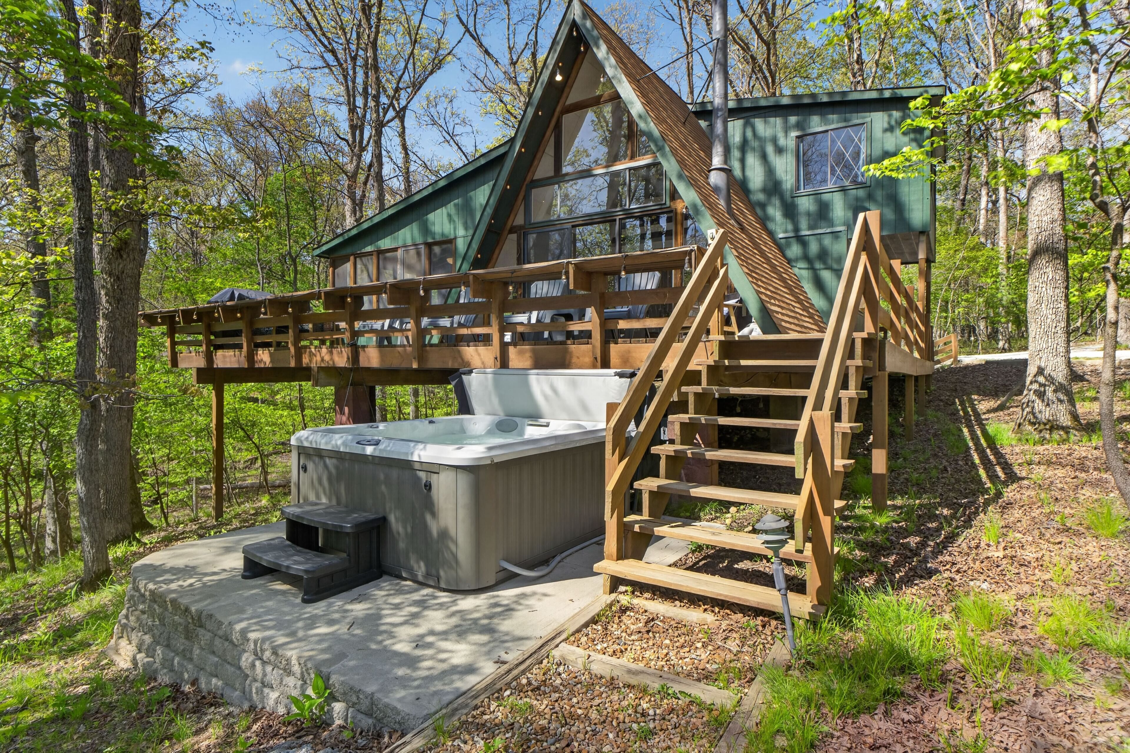 A cabin with a hot tub, wooden deck, and a staircase leading to a deck area.