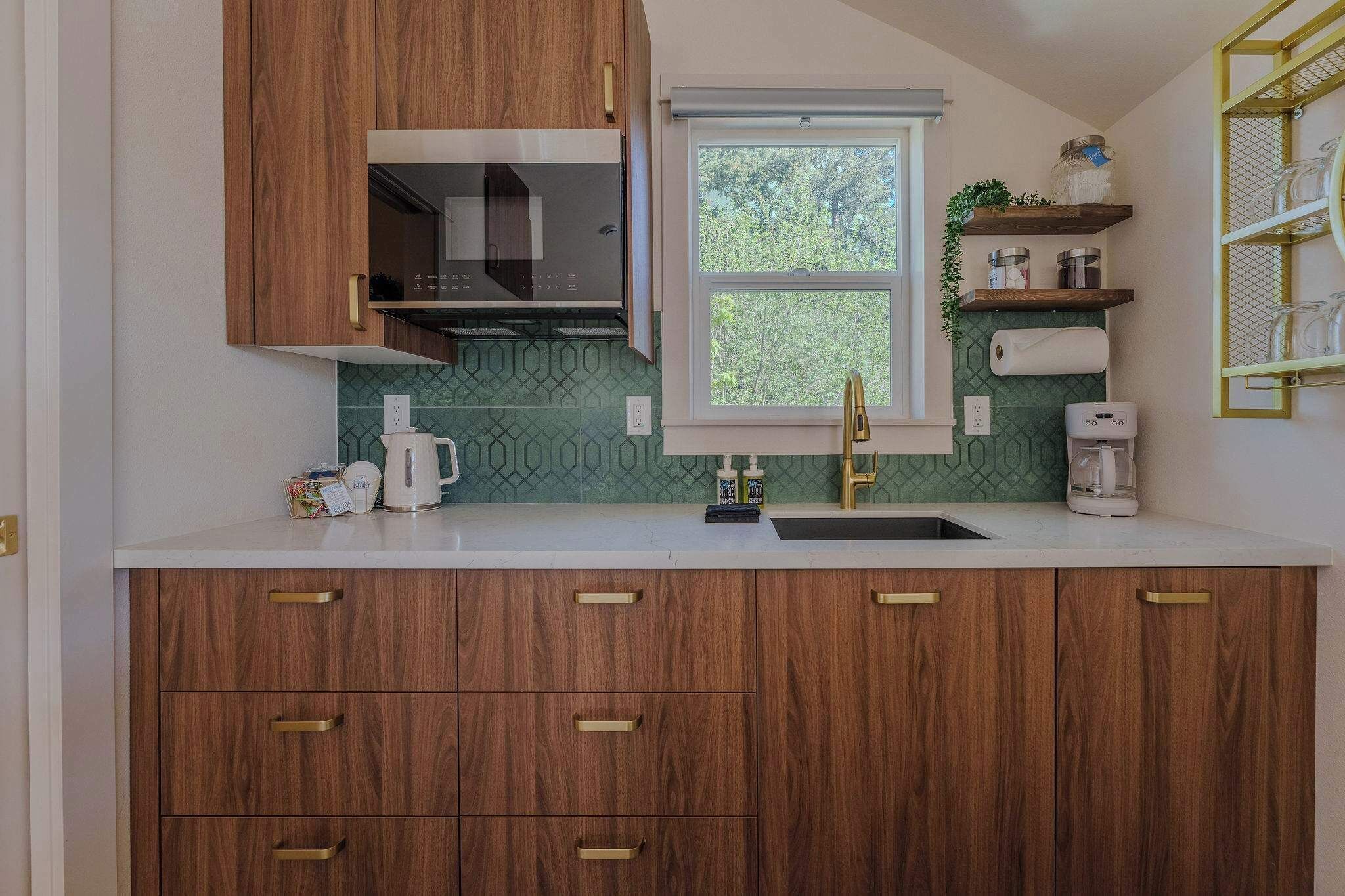 A kitchen with wooden cabinets, a built-in microwave, a window, and a countertop with a coffee maker.