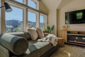 A modern living room with a large window, a sofa, a flat-screen TV, and a fish tank.