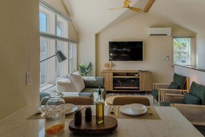 Ein Wohnzimmer mit einer Couch, einem Fernseher, einem Kamin und einem Essbereich mit Tisch für zwei Personen.
