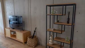 Ein Zimmer mit einem HolztV-Schrank, einem gewebten Korb und einem schwarzen Metallregal vor einer Holzwand.