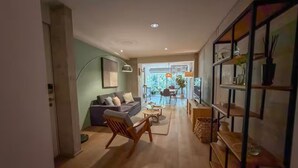 Ein modernes Wohnzimmer mit einer Couch, einem Sessel, einem Couchtisch, einem Bücherregal und einem Essbereich mit Stühlen und Tisch.