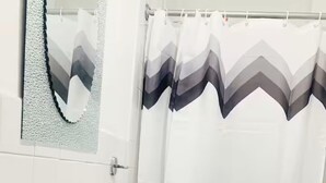 Een badkamer met een wit wastafelmeubel, een spiegel en een douchegordijn met een ruitpatroon.