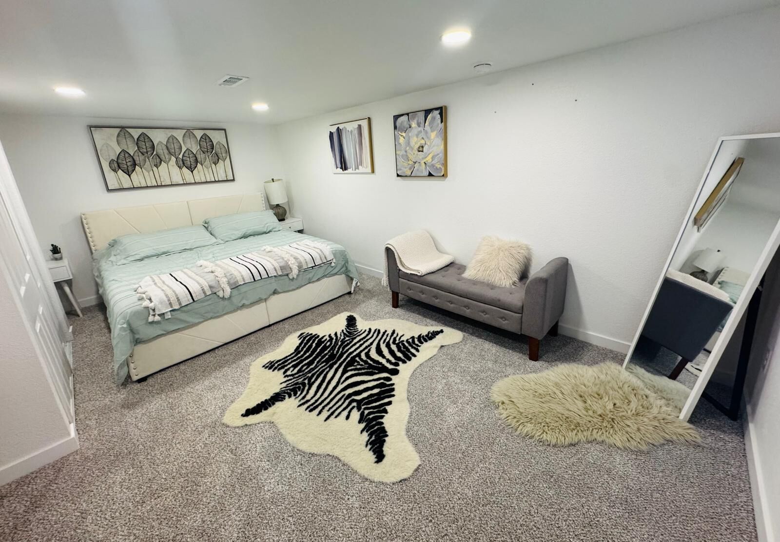 Un dormitorio con una cama, un sofá gris, una alfombra estampada de cebra y un espejo.