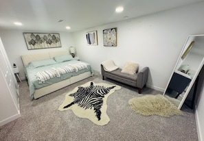 A bedroom with a bed, a grey sofa, a zebra rug, and a mirror.