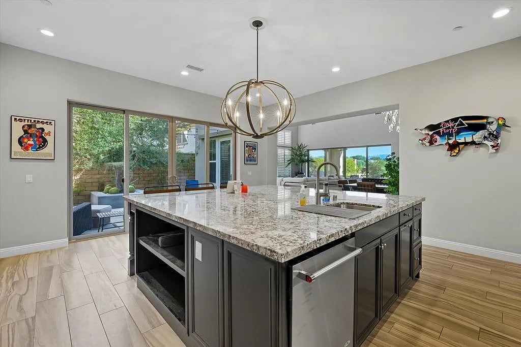 A modern kitchen with a large island, dark cabinetry, and a pendant light.