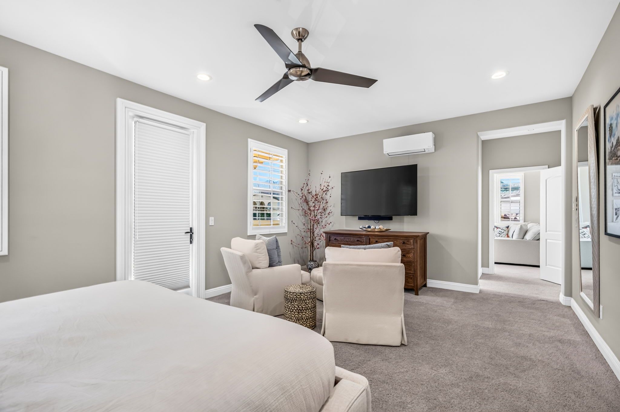 A bedroom with a bed, a TV, a ceiling fan, and a view of the outside through a window.