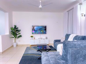Un salon moderne avec un téléviseur à écran plat, un ventilateur de plafond, un canapé, une table basse, une plante en pot et un meuble blanc.