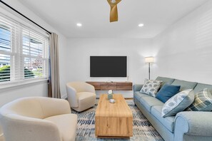 Ein modernes Wohnzimmer mit Sofa, Sessel, Couchtisch und einem an der Wand befestigten Flachbildfernseher.