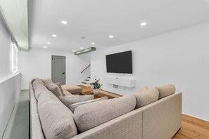 Ein modernes Wohnzimmer mit einem großen Ecksofa, einem flachbildfernseher an der Wand, einem Couchtisch aus Holz und einer Treppe, die zu einer weiteren Ebene führt.