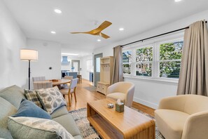 Ein modernes Wohnzimmer mit Sofa, Sessel, Couchtisch aus Holz und Deckenventilator.