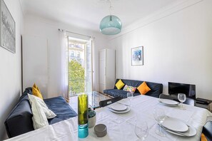 A modern hotel room with a balcony, a dining table set with plates and glasses, a sofa with colorful cushions, and a television on a stand. - Warm Apartment 2P in the Heart of Nice - Near the sea (Nice)