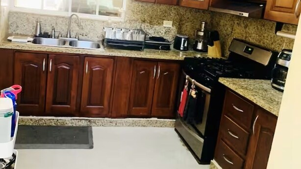 A kitchen with wooden cabinets, a stainless steel sink, a stove, and a window.