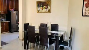 A dining area with a table and chairs, a clock on the wall, and a painting above the table.