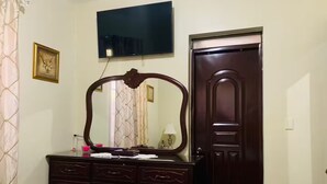 A bedroom with a bed, a dresser with drawers, a large mirror, a television mounted on the wall, and a door.