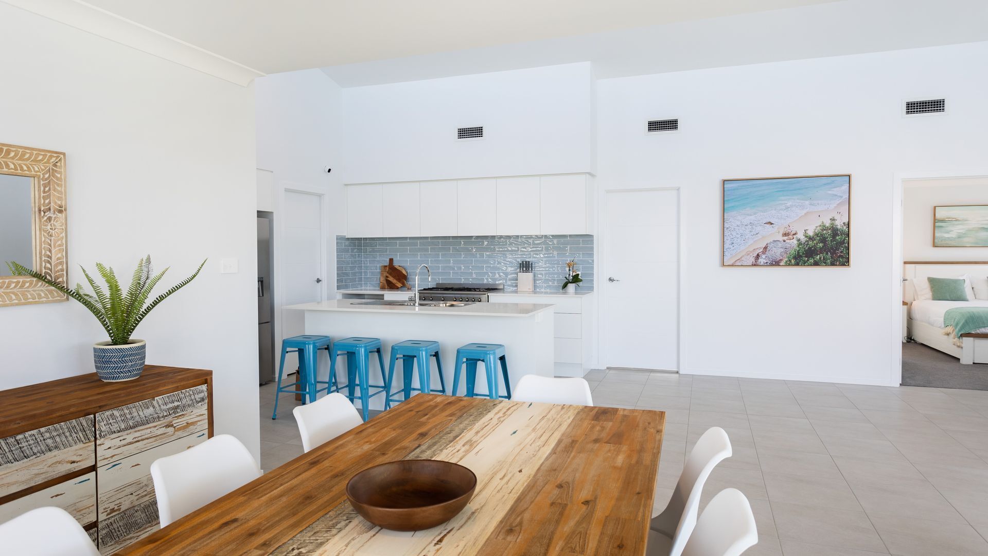 A modern kitchen with white cabinets, a blue backsplash, and a central island with stools.