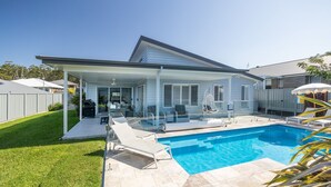 Ett modernt hus med en täckt uteplats, en swimmingpool och en välskött gräsmatta.