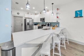 A modern kitchen with white cabinetry, stainless steel appliances, and a central island with bar stools. - Mermaid Manor (Panama City Beach)