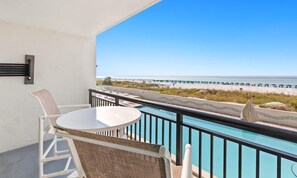 A balcony with a pool, a table, and chairs, overlooking a beach and a pier. - Sundestin 205 (Destin)