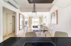 Een moderne eetruimte met een glazen tafel en stoelen, een zwart marmeren aanrechtblad en een plafondventilator.