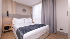 A modern hotel room with a bed, a bedside table, a wall-mounted light, a window with curtains, and a wall clock. - Jatisa 603 in Medell n (Medellín)