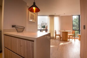 Une cuisine moderne dotée d’un îlot central, d’un coin repas avec une table ronde et des chaises, et d’une grande fenêtre offrant une vue sur les bâtiments.