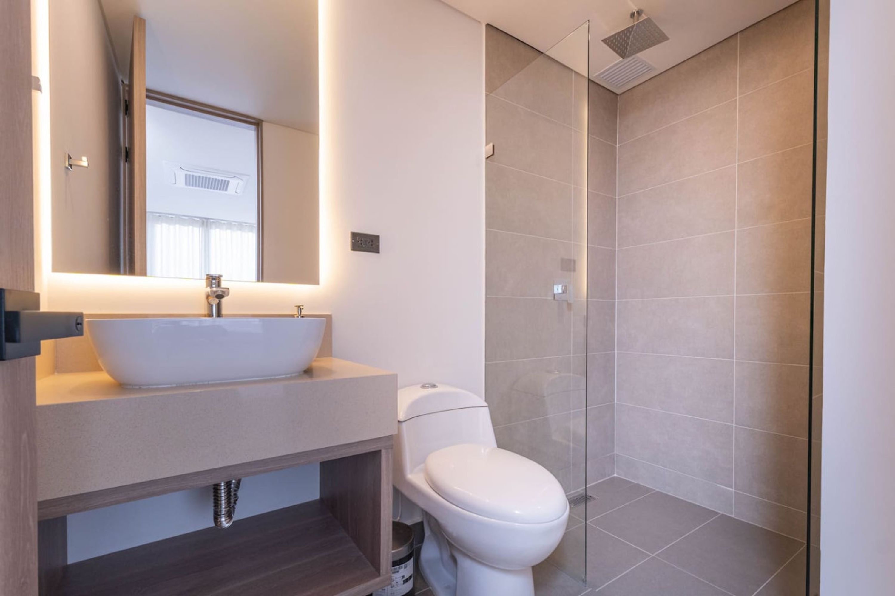 Een moderne badkamer met een wastafel op voet, toilet en douche met glazen wanden.