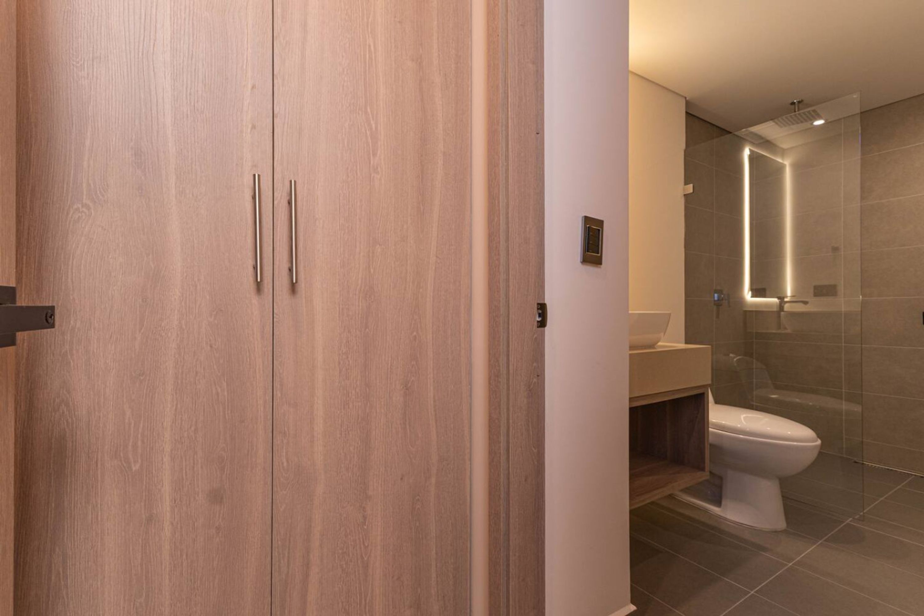 A modern bathroom with a wooden cabinet, a glass shower enclosure, and a white toilet.