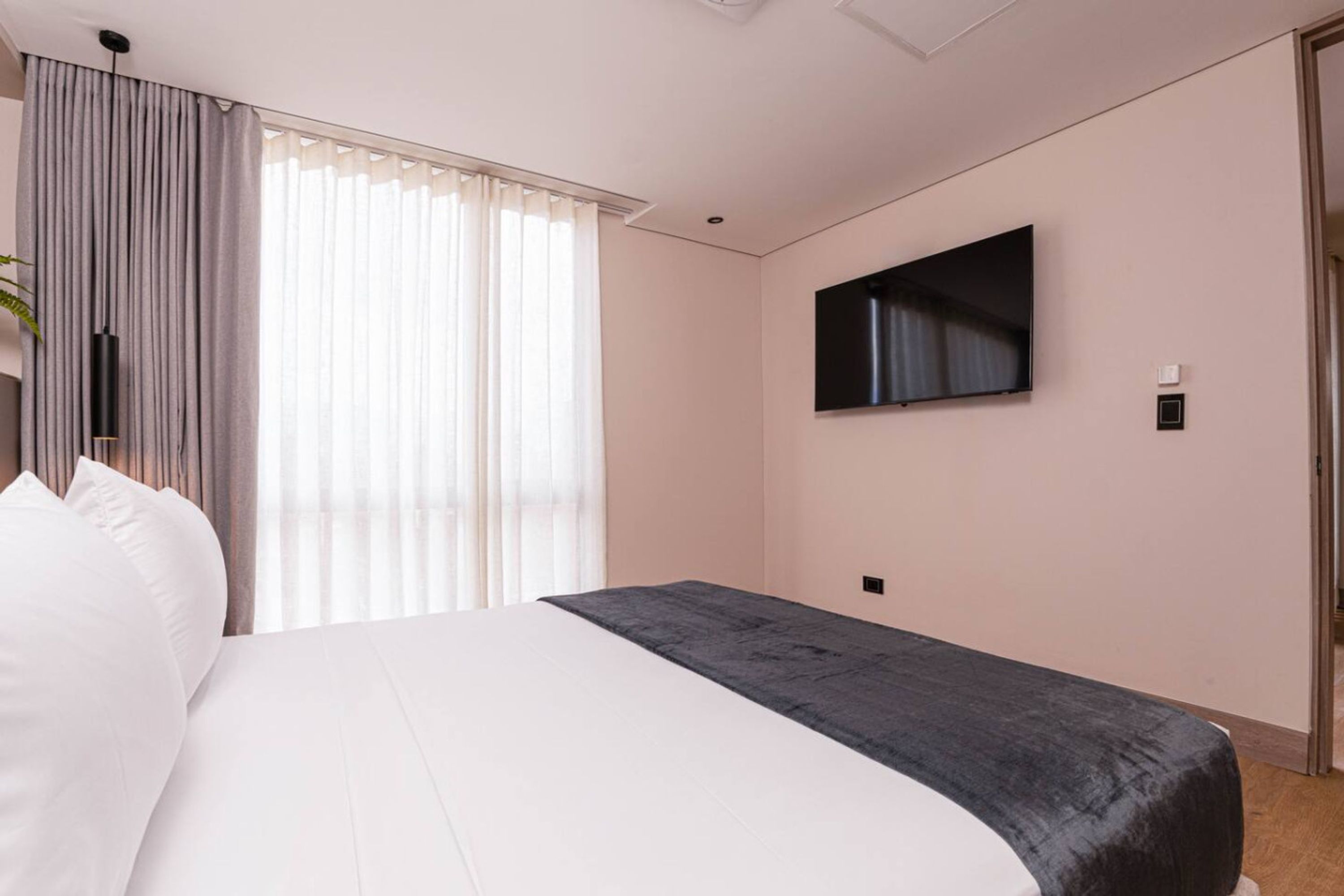 A hotel room with a bed, a TV mounted on the wall, and a window with curtains.