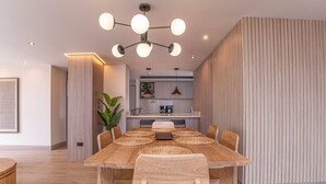 Ein moderner Essbereich mit einem Holztisch und Stühlen, im Hintergrund eine Küche und rechts eine vertikale Holzverkleidung.