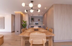 A modern dining area with a wooden table and chairs, a kitchen in the background, and a vertical wooden panel on the right. - Jatisa 1001 in Medell n (Medellín)