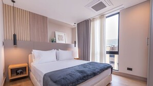 Ein modernes Hotelzimmer mit einem großen Bett, einem Nachttisch, einem Wandregal und einem Fenster mit Vorhängen.