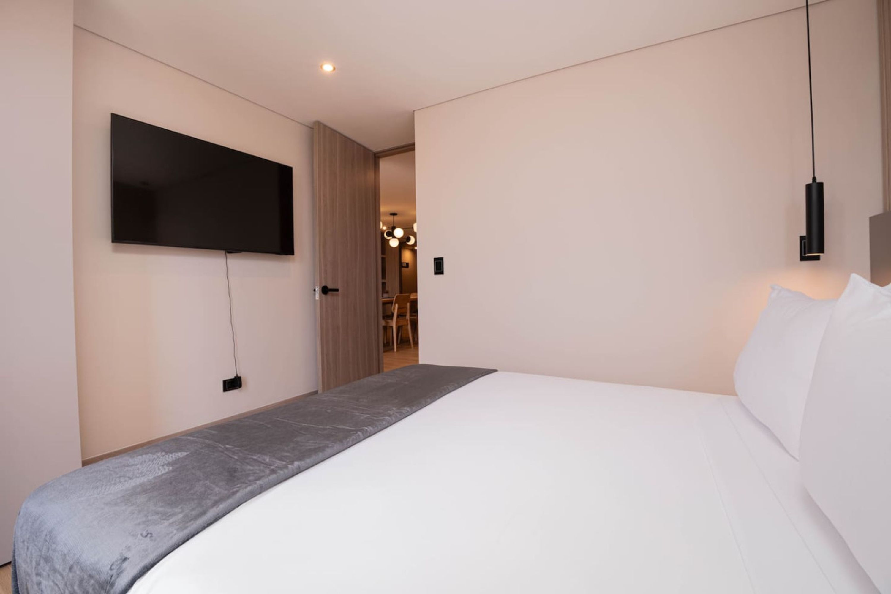 A bedroom with a bed, a TV mounted on the wall, and a door leading to another room.
