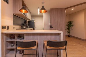 Eine moderne Küche mit einer zentralen Kochinsel, zwei Barhocker, Pendelleuchten und einem Blumentopf.