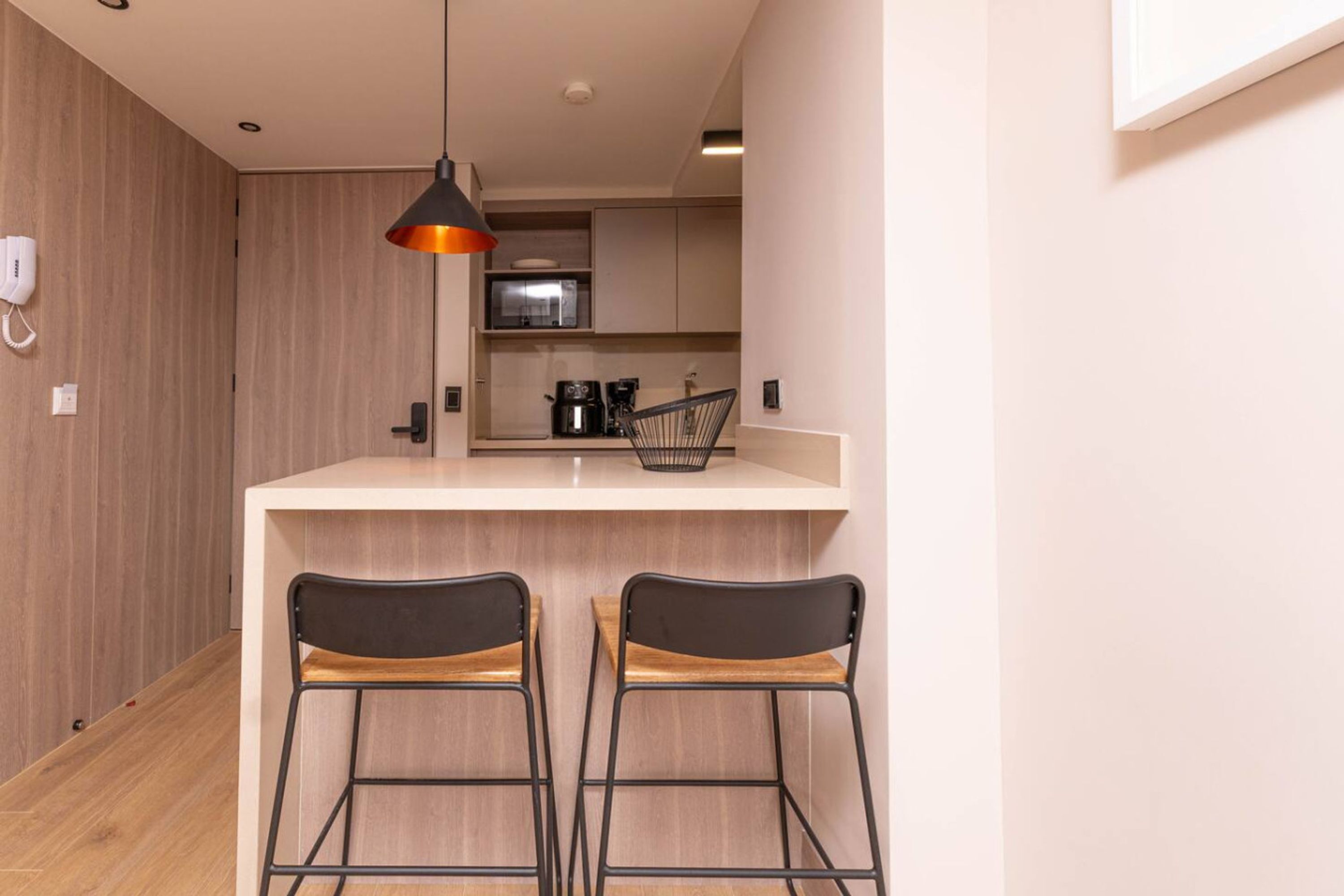 Une cuisine moderne avec un plan de travail blanc, deux chaises noires, un luminaire suspendu et un four à micro-ondes.